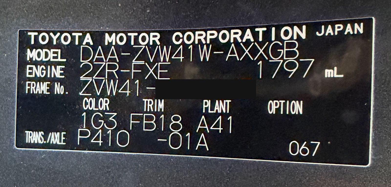 Toyota model plate showing the model code, engine, frame number with the last digits covered, and the colour, trim and plant codes