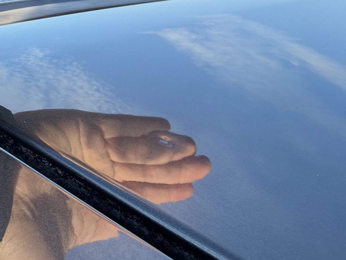 Roof panel reflecting a hand; the reflection bends at one point where the dent is