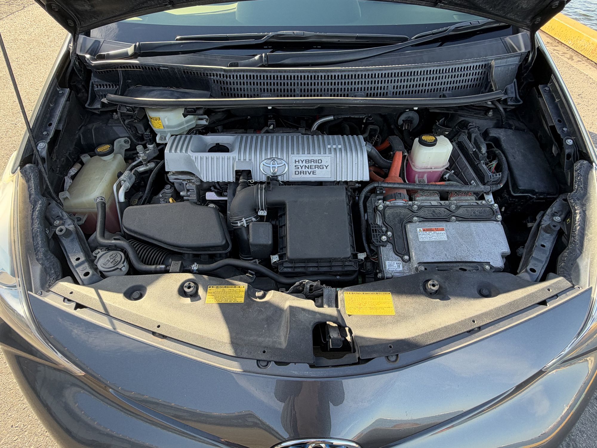 Engine bay of a grey Toyota Prius α with the bonnet open, seen from the front